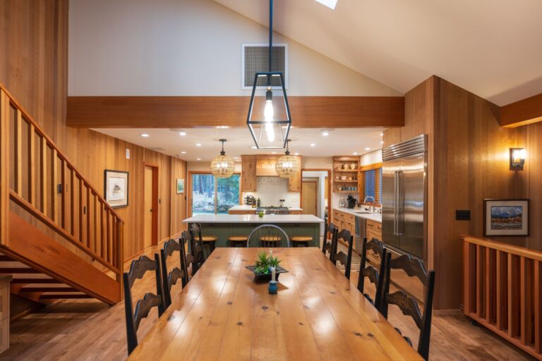A bright, open dining and kitchen area featuring a spacious wooden table, custom cabinetry, and statement lighting for a warm, inviting atmosphere.