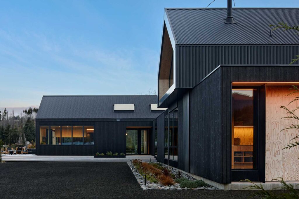 A contemporary residential compound featuring black vertical siding and softly lit interiors at dusk.