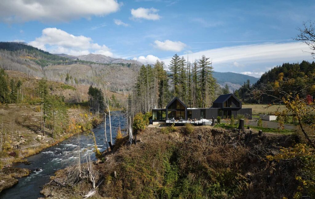A contemporary riverfront residence positioned within a forested mountain landscape.