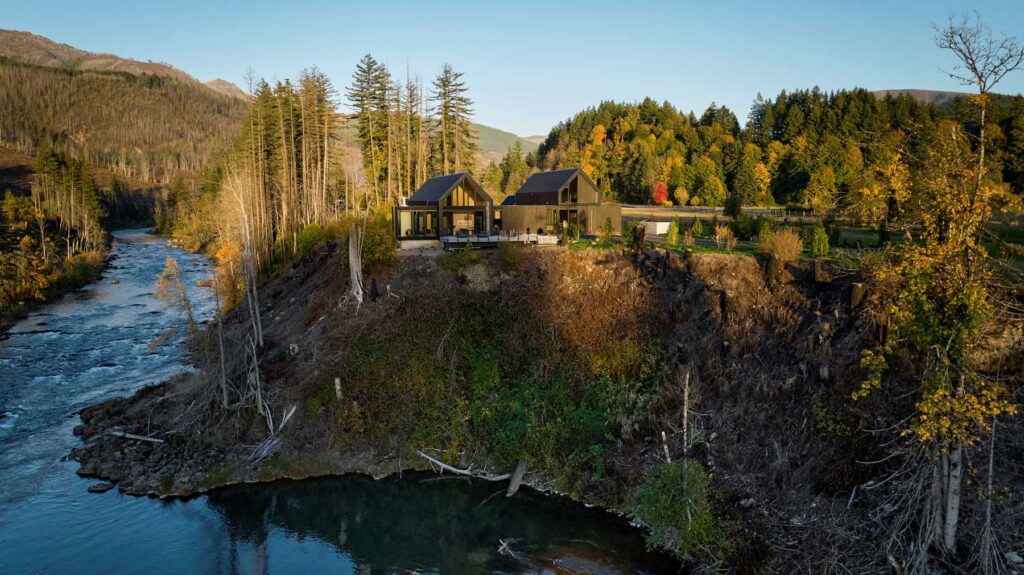 Aerial perspective of modern homes situated on a cliff above a river, surrounded by forested terrain.