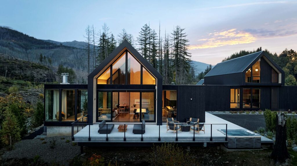 Aerial view of modern gabled homes with expansive glazing and outdoor living spaces overlooking a river.