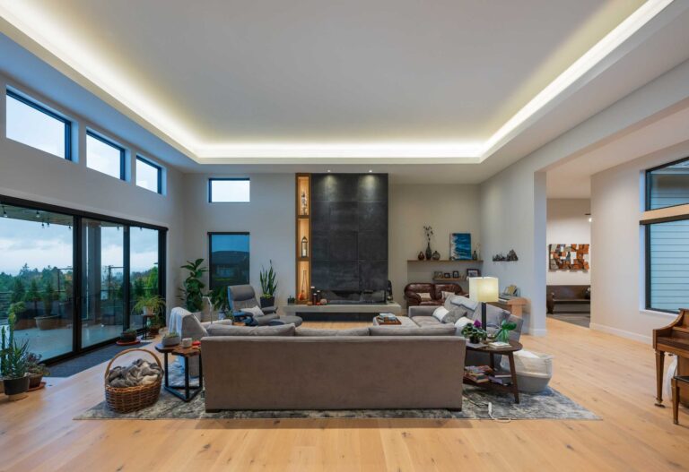 A bright, open living space featuring a tray ceiling with ambient lighting, expansive windows, and elegant modern furnishings.