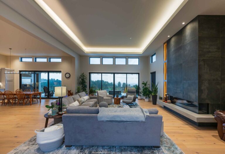 A stylish living space featuring a sleek fireplace, tray ceiling lighting, and expansive windows for natural light and scenic views.