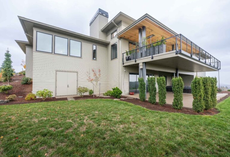 A striking custom home featuring expansive windows and a spacious elevated deck with cable railing for panoramic views.