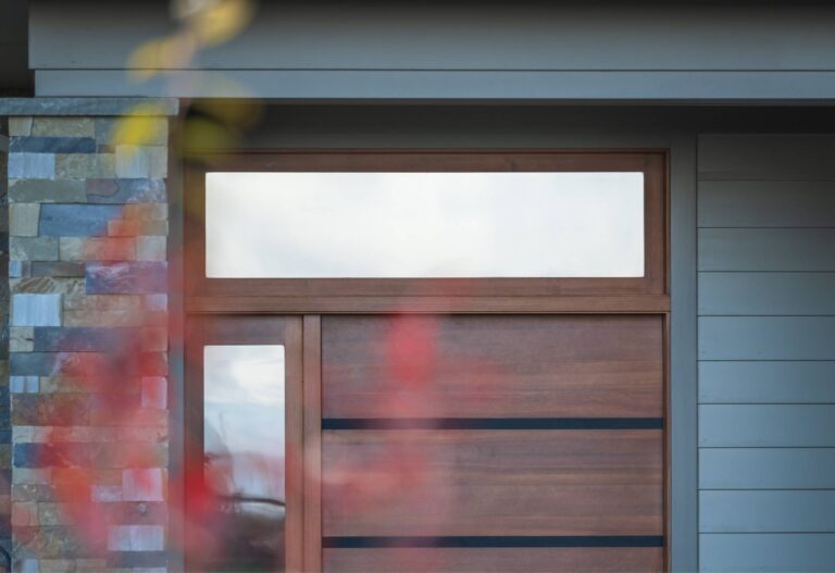 Elegant wood entry door with sleek horizontal accents and a transom window, complemented by natural stone siding.