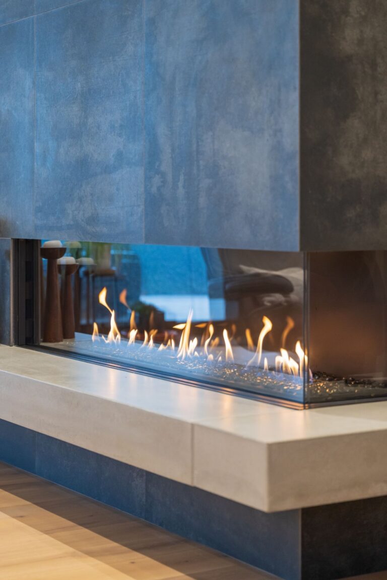 A sleek linear gas fireplace with glass enclosure and dark stone finish adds warmth and style to this custom home.