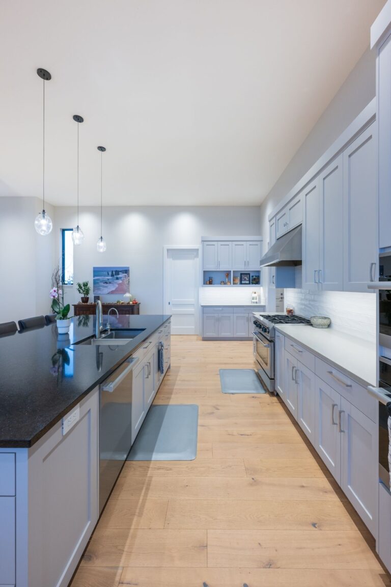 A sleek kitchen design featuring light gray cabinets, a spacious island with black countertop, and elegant pendant lights.