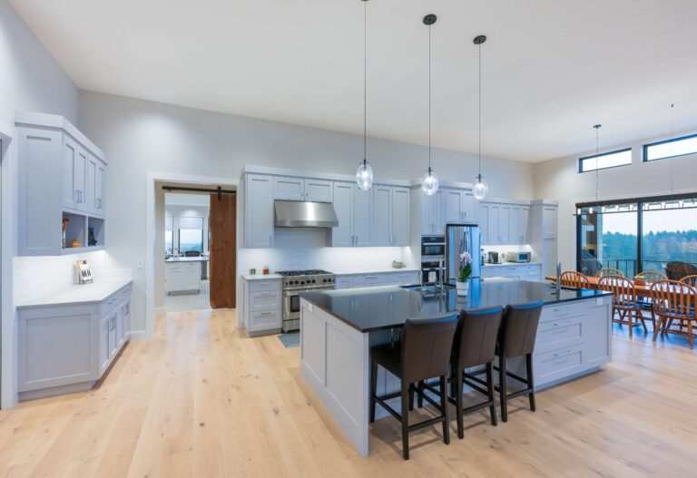 A bright, open kitchen featuring elegant gray cabinets, a sleek black island countertop, and warm hardwood flooring.